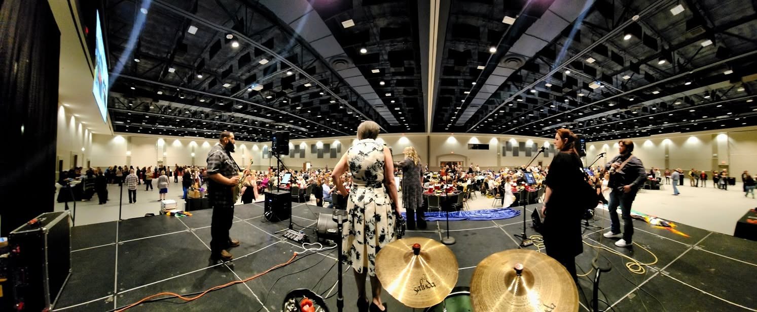 Seasoned by Fire on stage in a large hall, drums in front, people seated at tables.